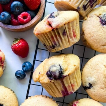 An array of mixed berry muffins on a wire rack.