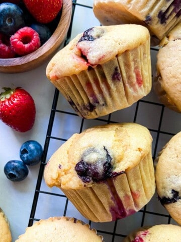 An array of mixed berry muffins on a wire rack.