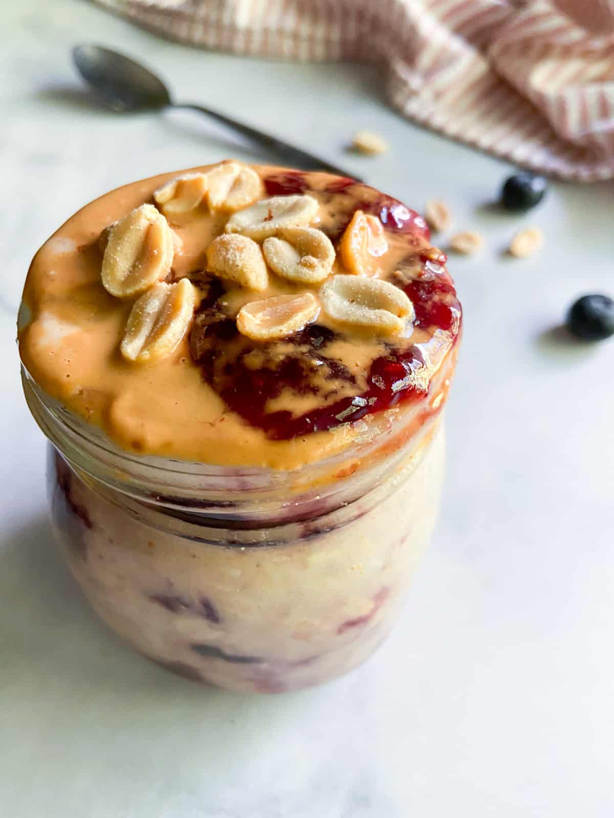 A jar of pb and j overnight oats garnished with peanuts.