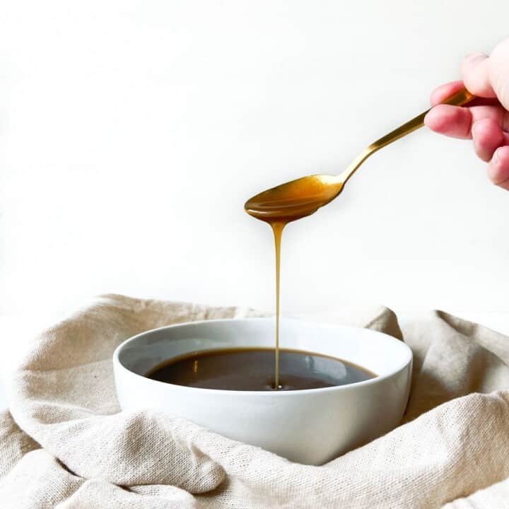 A hand pouring caramel sauce into a bowl with a spoon.