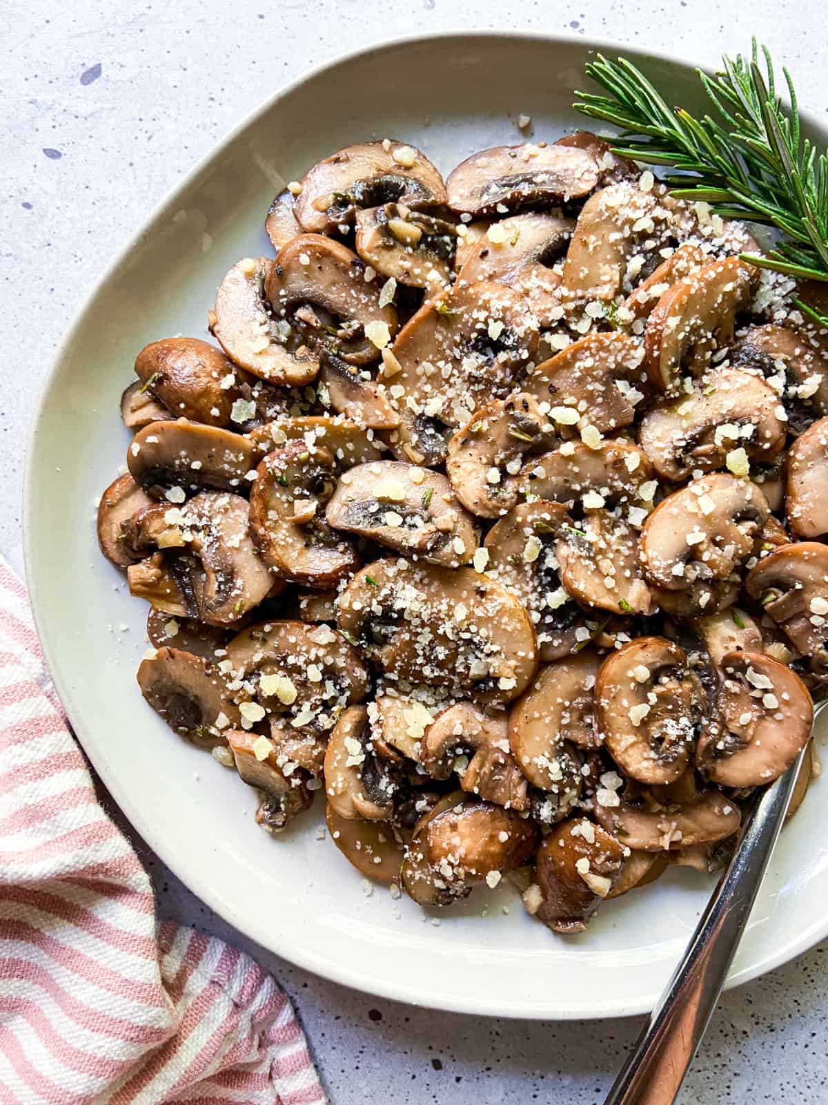A plate of garlic butter mushrooms with a sprig of rosemary.