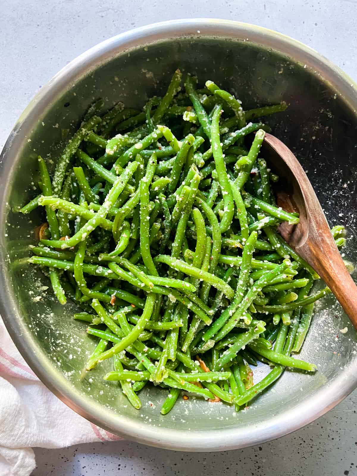A bowl of green beans tossed with garlic olive oil, crushed red pepper flakes, and parmesan cheese.