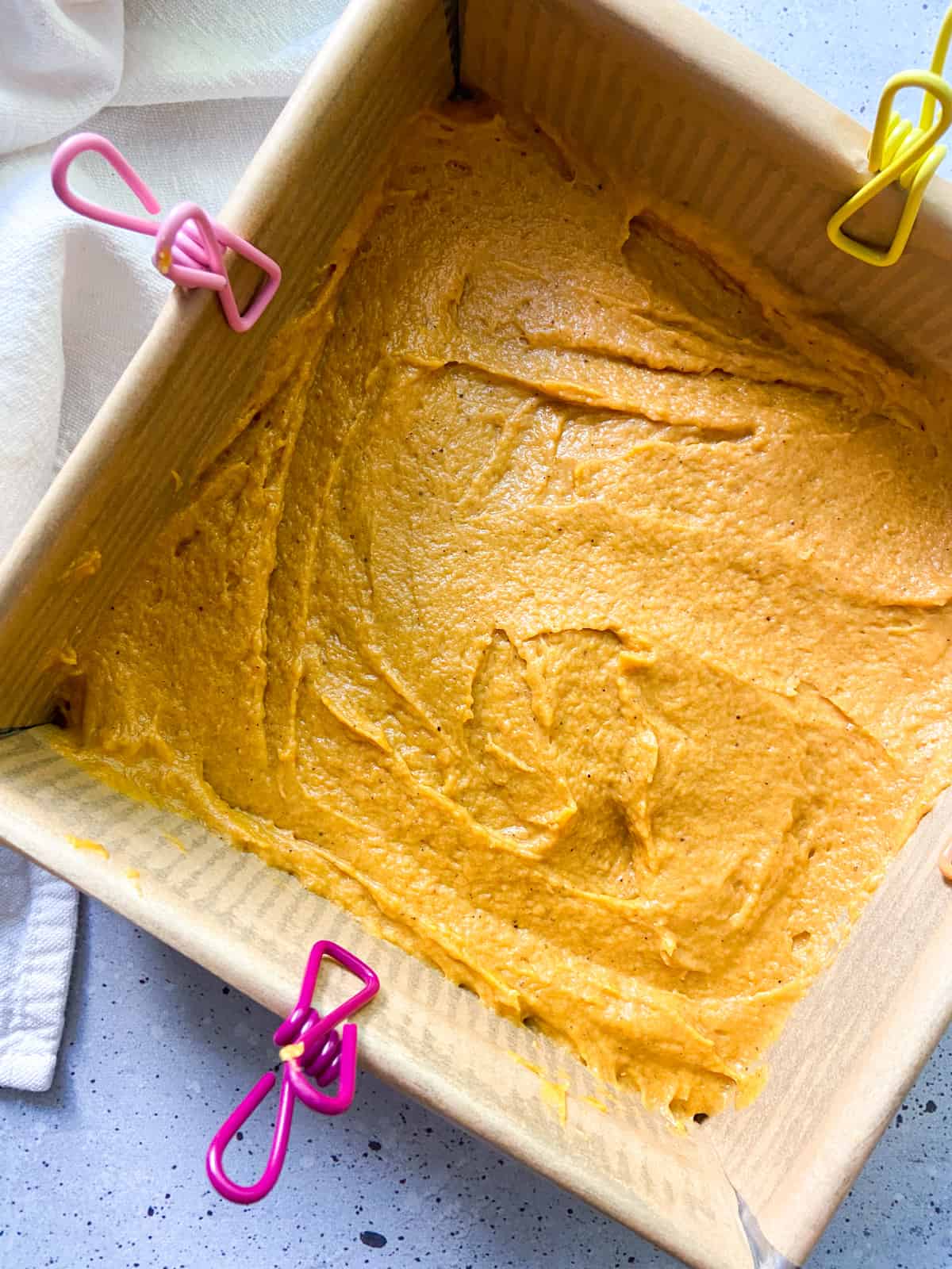 Pumpkin cake batter spread into the base of a parchment-lined baking pan.