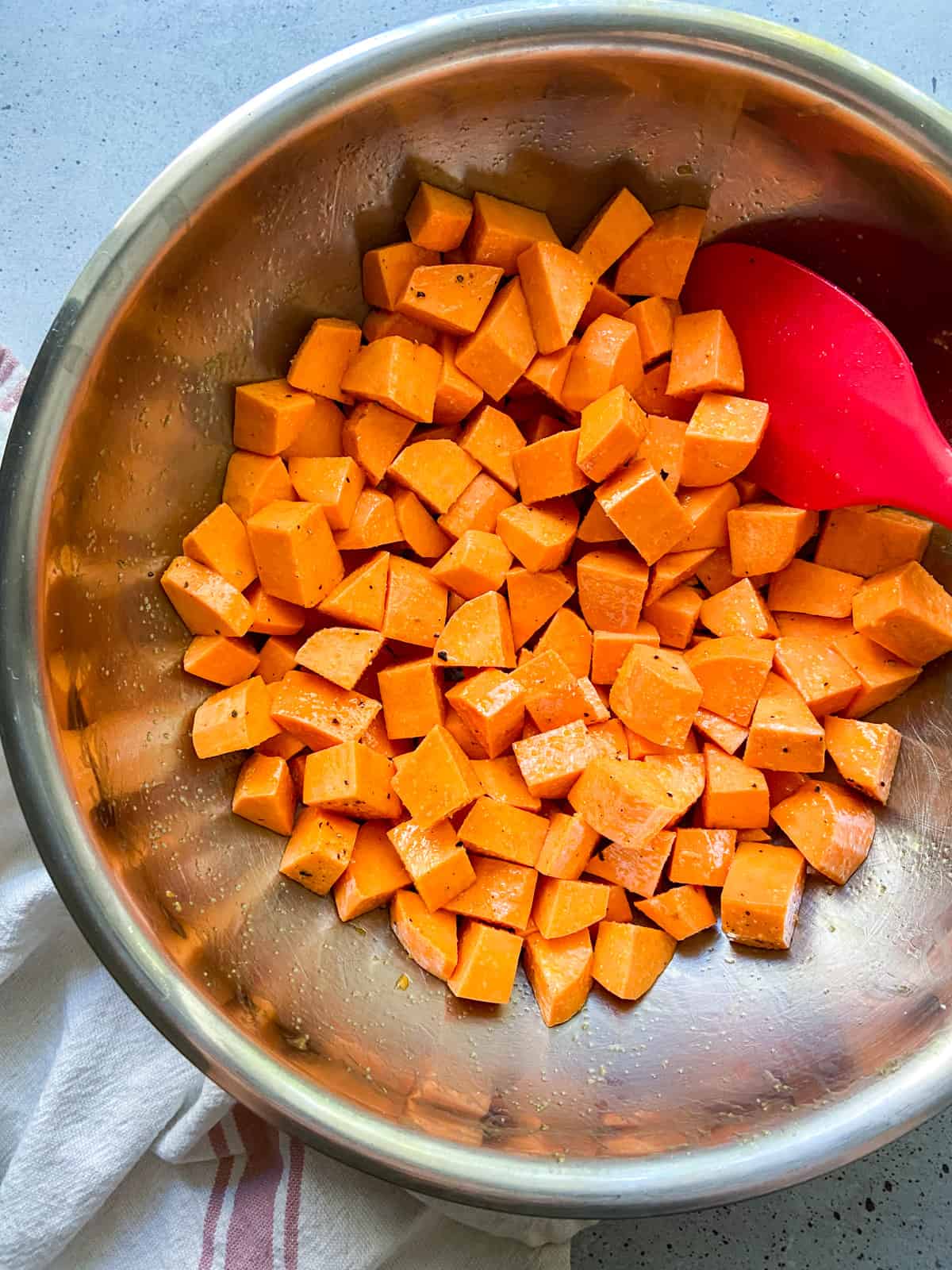 Raw diced sweet potatoes coated in olive oil in a bowl.
