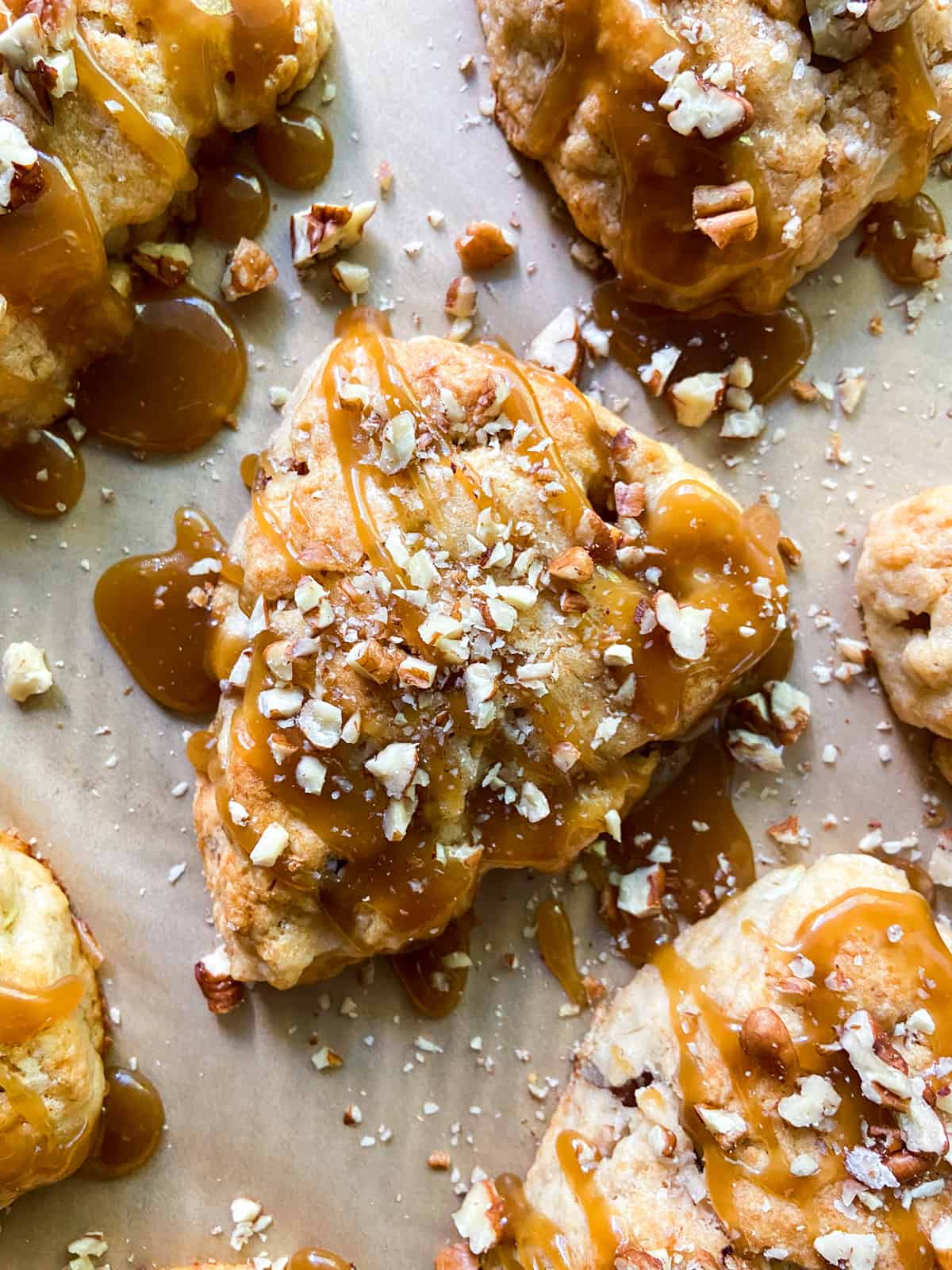 An apple scone with caramel glaze and chopped pecan garnish.