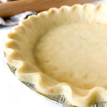 An unbaked all-butter pie crust with a fluted edge in a foil pie tin.