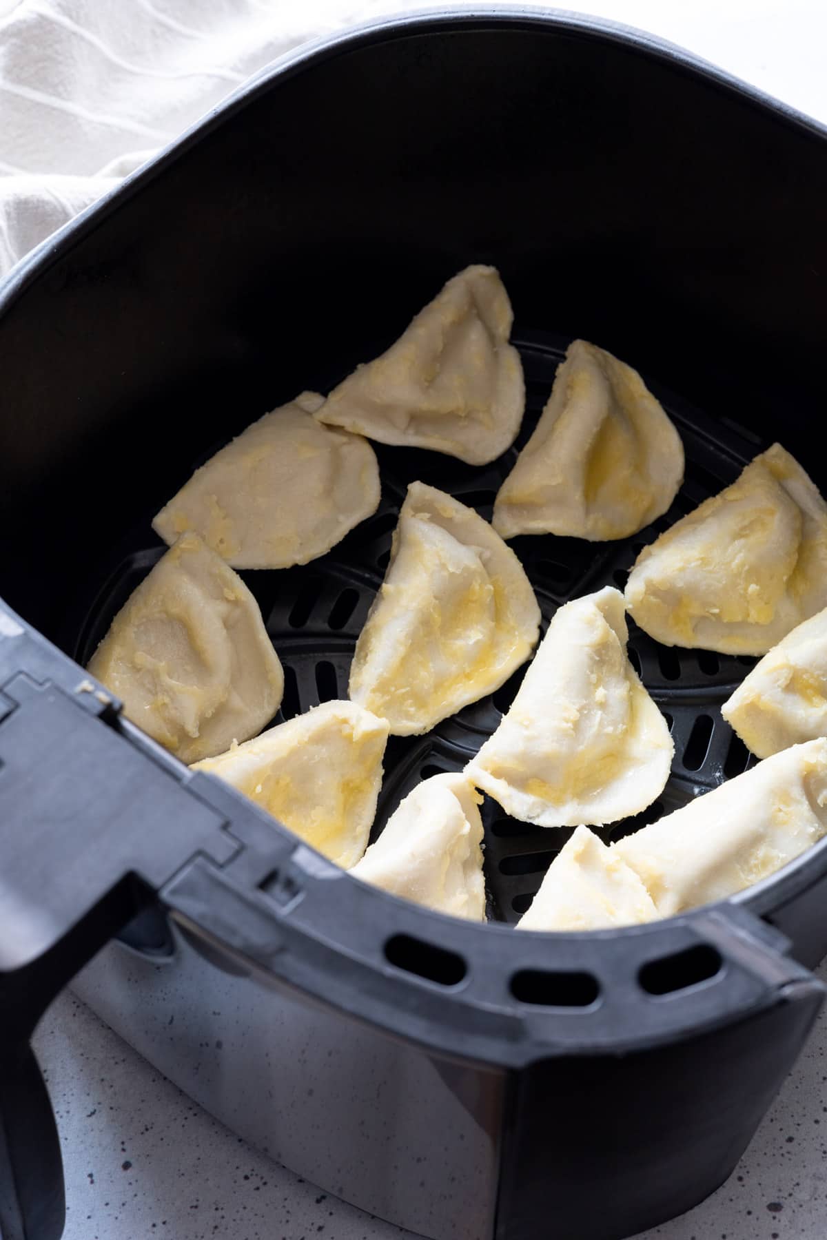 Butter slathered uncooked pierogies in the basket of an air fryer.