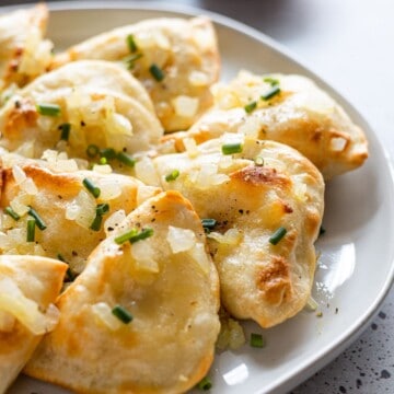 A plate of pierogies garnished with onions.