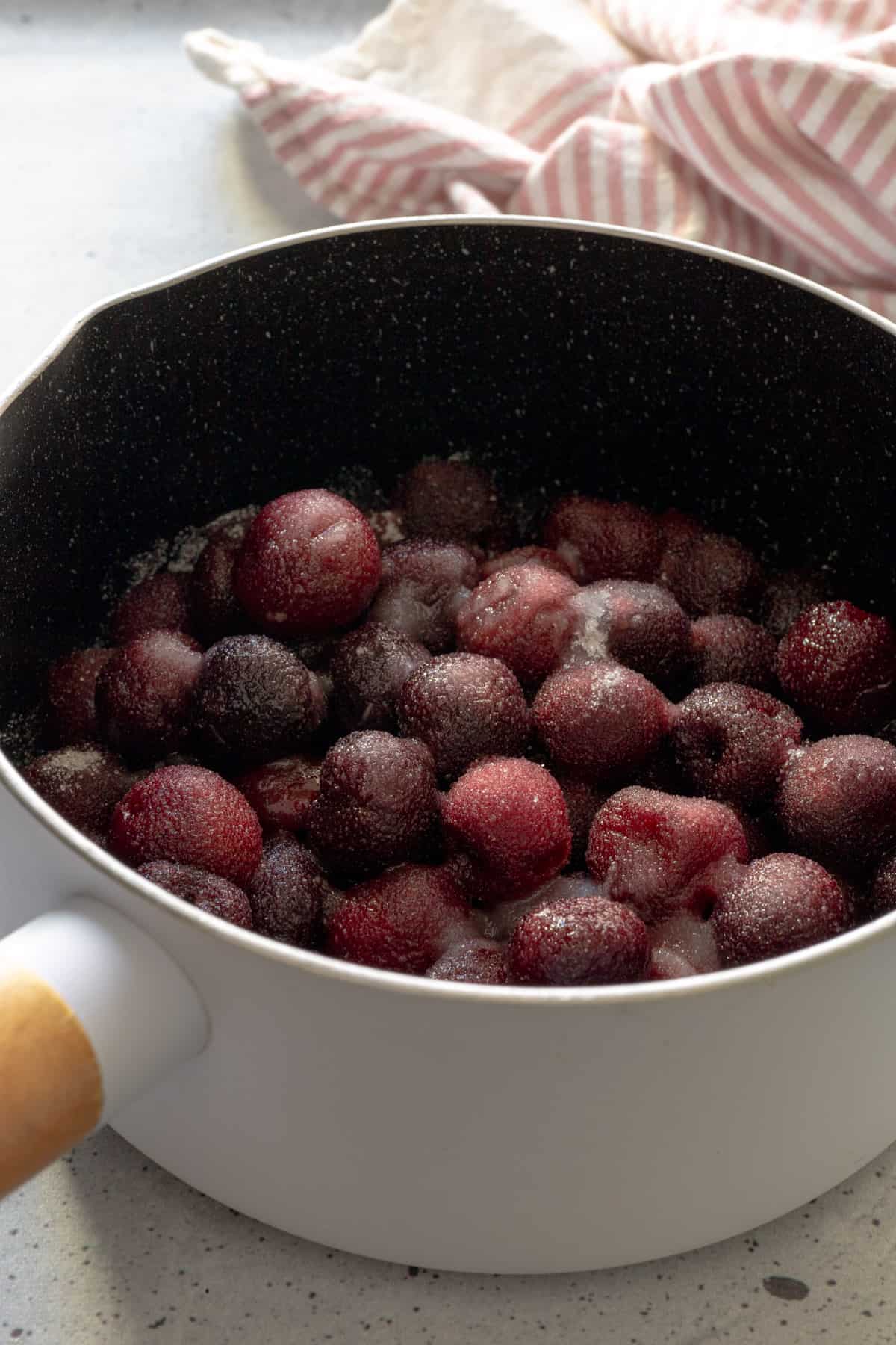 Cherries covered in sugar and lemon juice in a small saucepan.