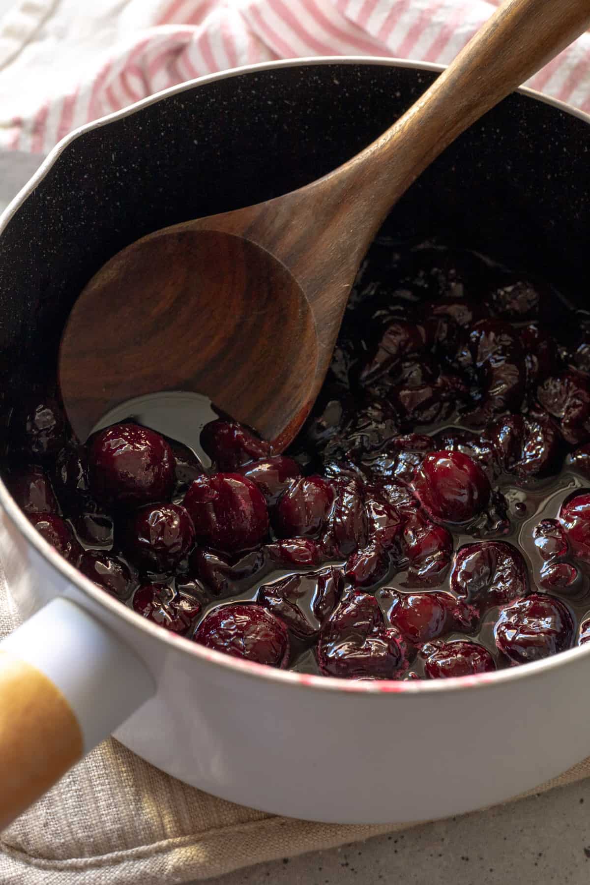 A saucepan filled with cooked cherry compote and a wooden spoon.