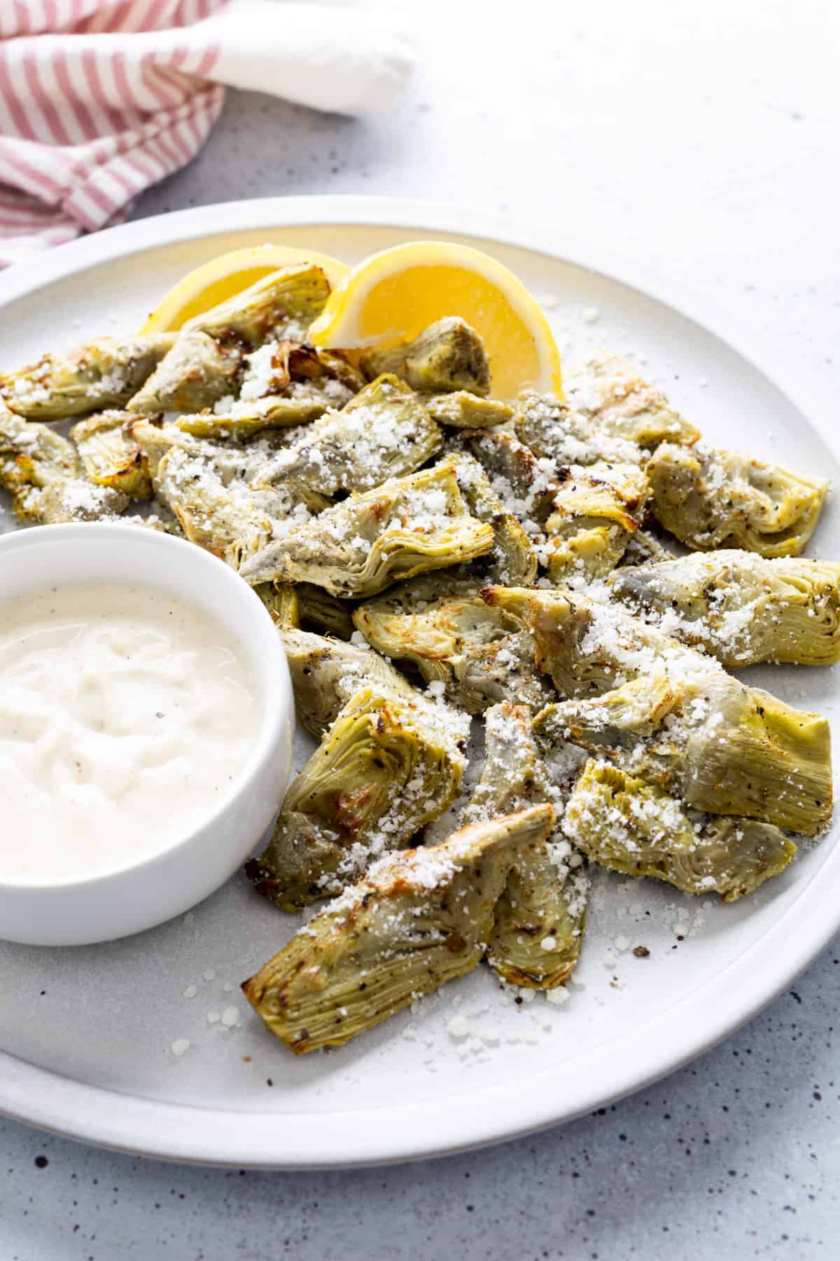 A plate of air-fried artichoke hearts garnished with parmesan cheese with a side of garlic aioli sauce.
