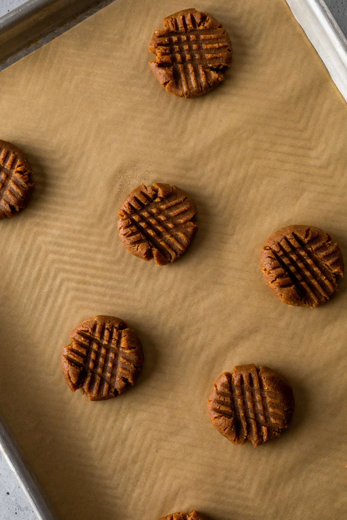 Balls of cookie dough smashed down with a fork in a criss-cross pattern on a parchment-lined tray.