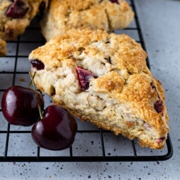 A cherry scone on a wire cooling rack with fresh cherries.