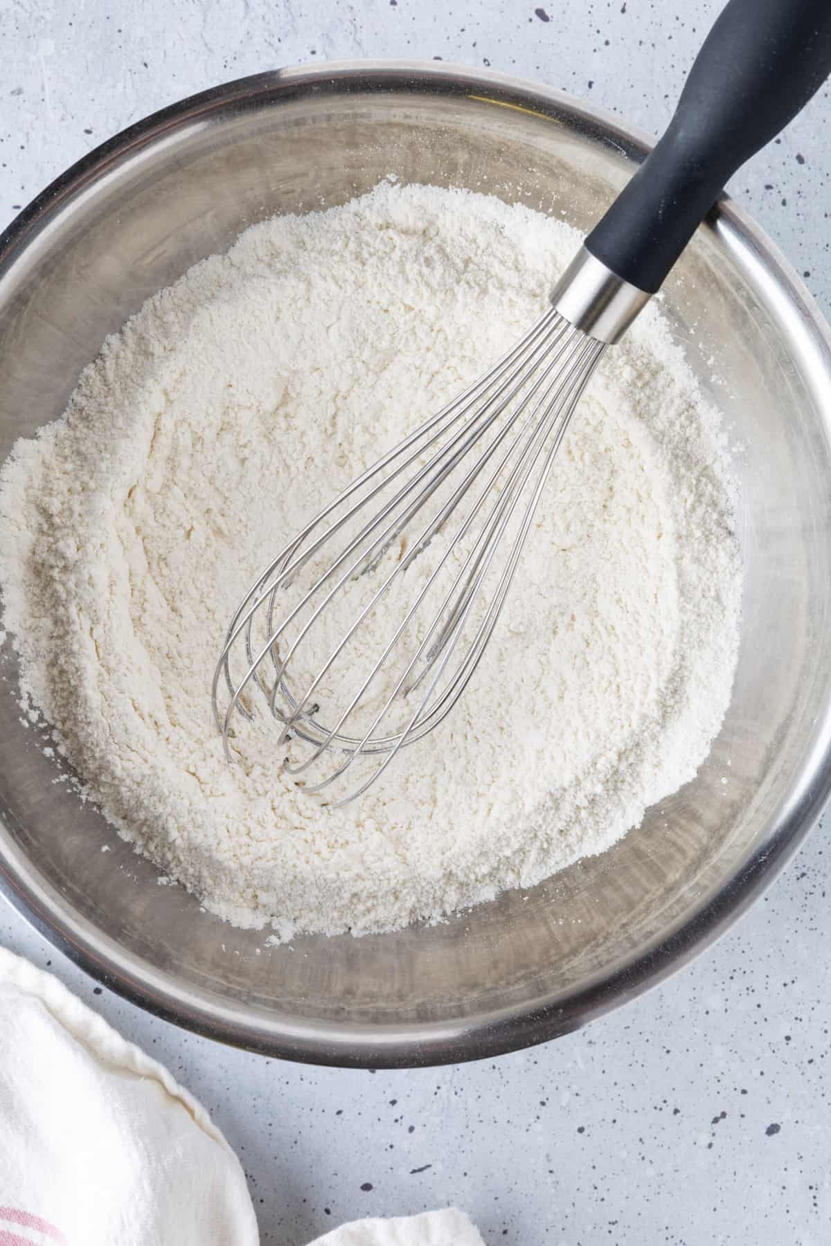 A bowl of dry ingredients with a whisk.
