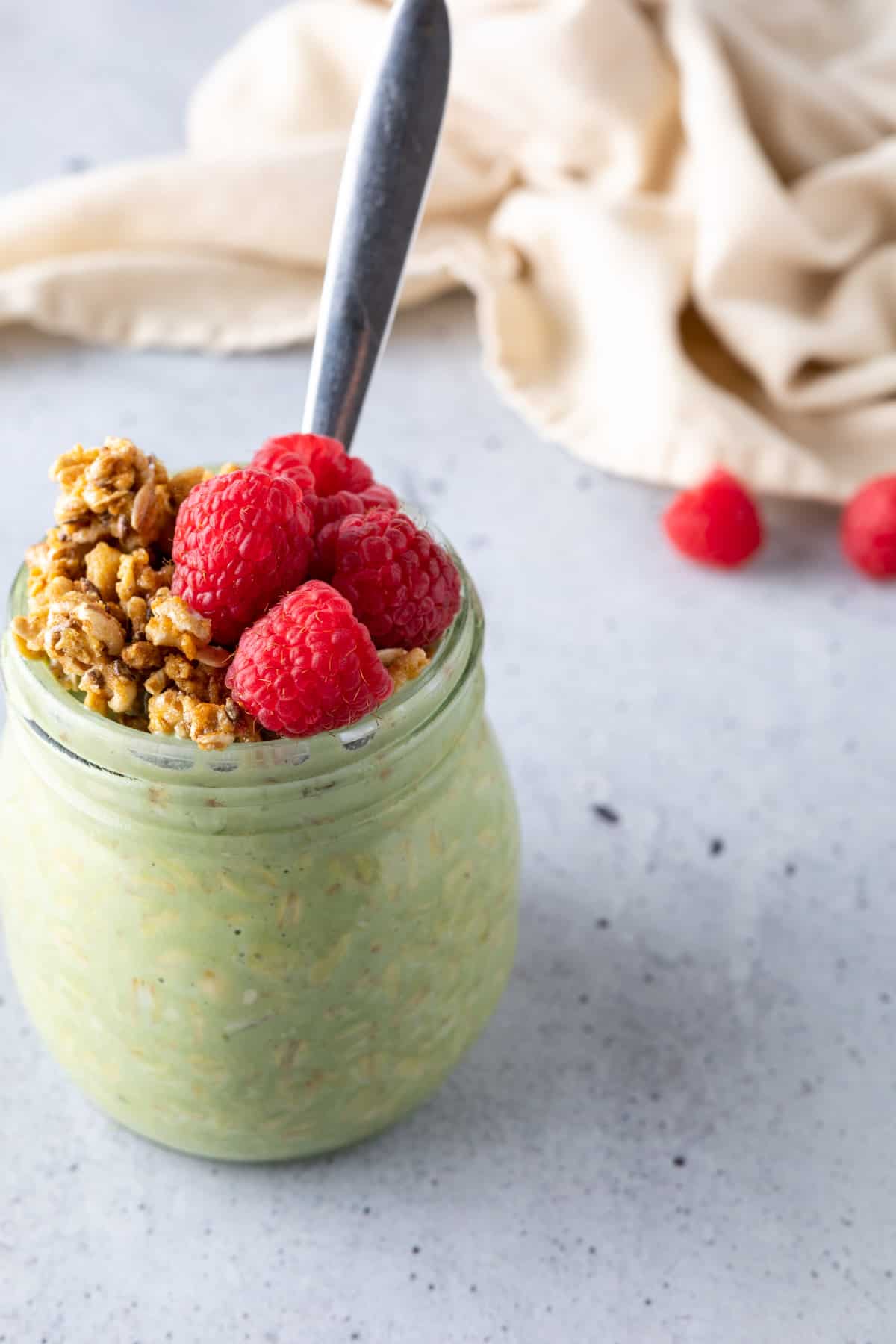 Matcha overnight oats in a jar with fresh raspberries, granola, and a spoon.