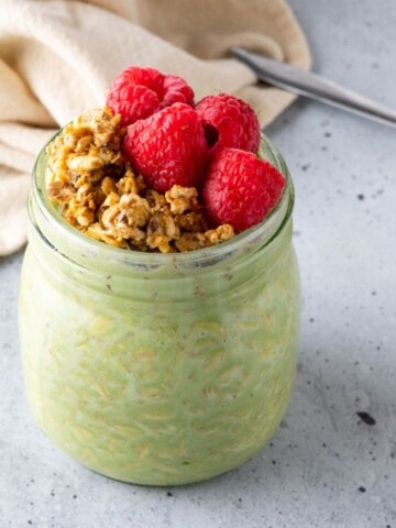 A jar of matcha overnight oats topped with granola and raspberries.