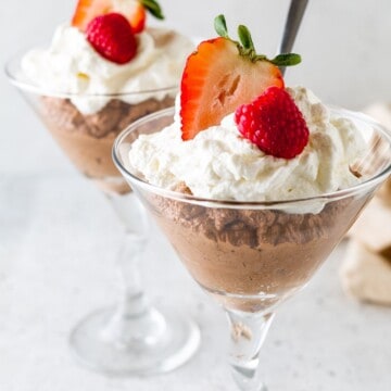 Whipped cream topped chocolate mousse in martini glasses.