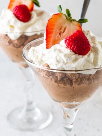 Whipped cream topped chocolate mousse in martini glasses.