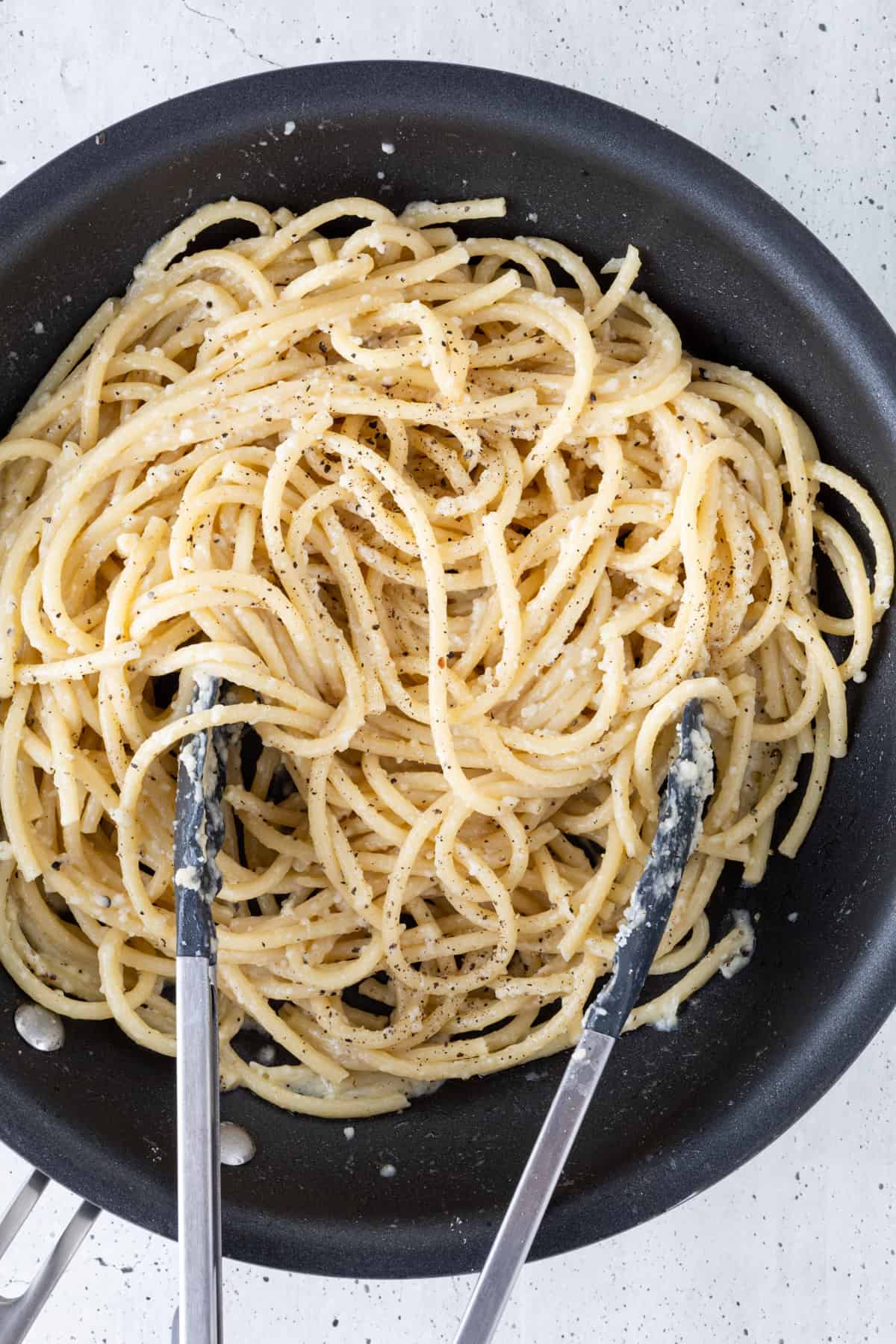 Cacio e Pepe pasta in a skillet with large tongs.