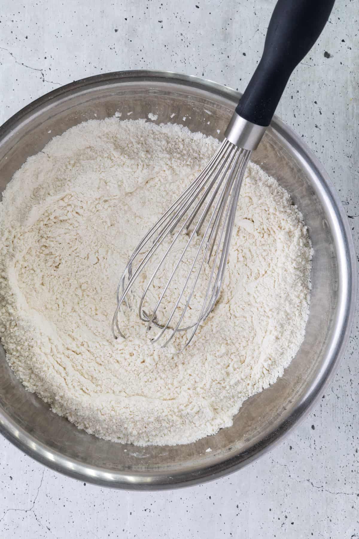 Dry ingredients in a mixing bowl with a large whisk.