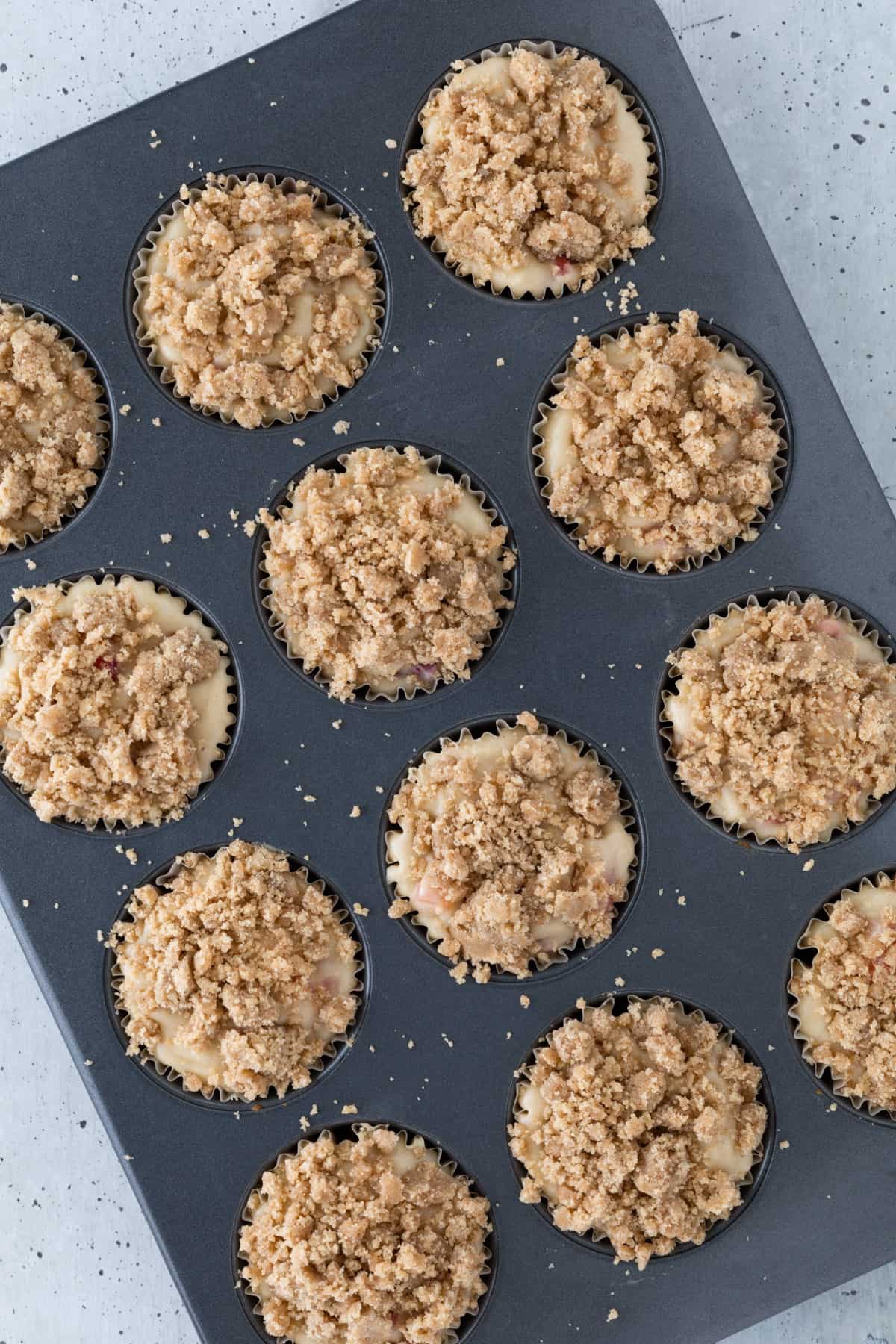 Streusel-covered unbaked muffins in a muffin pan.