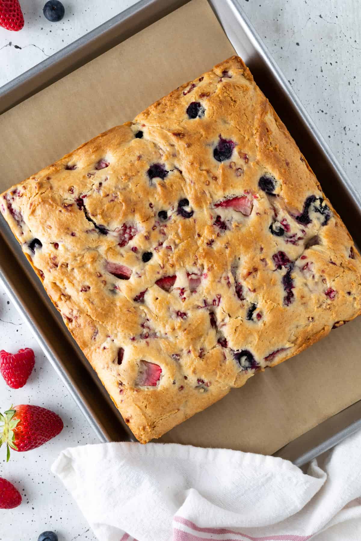 An unfrosted mixed berry cake on a parchment-lined tray.