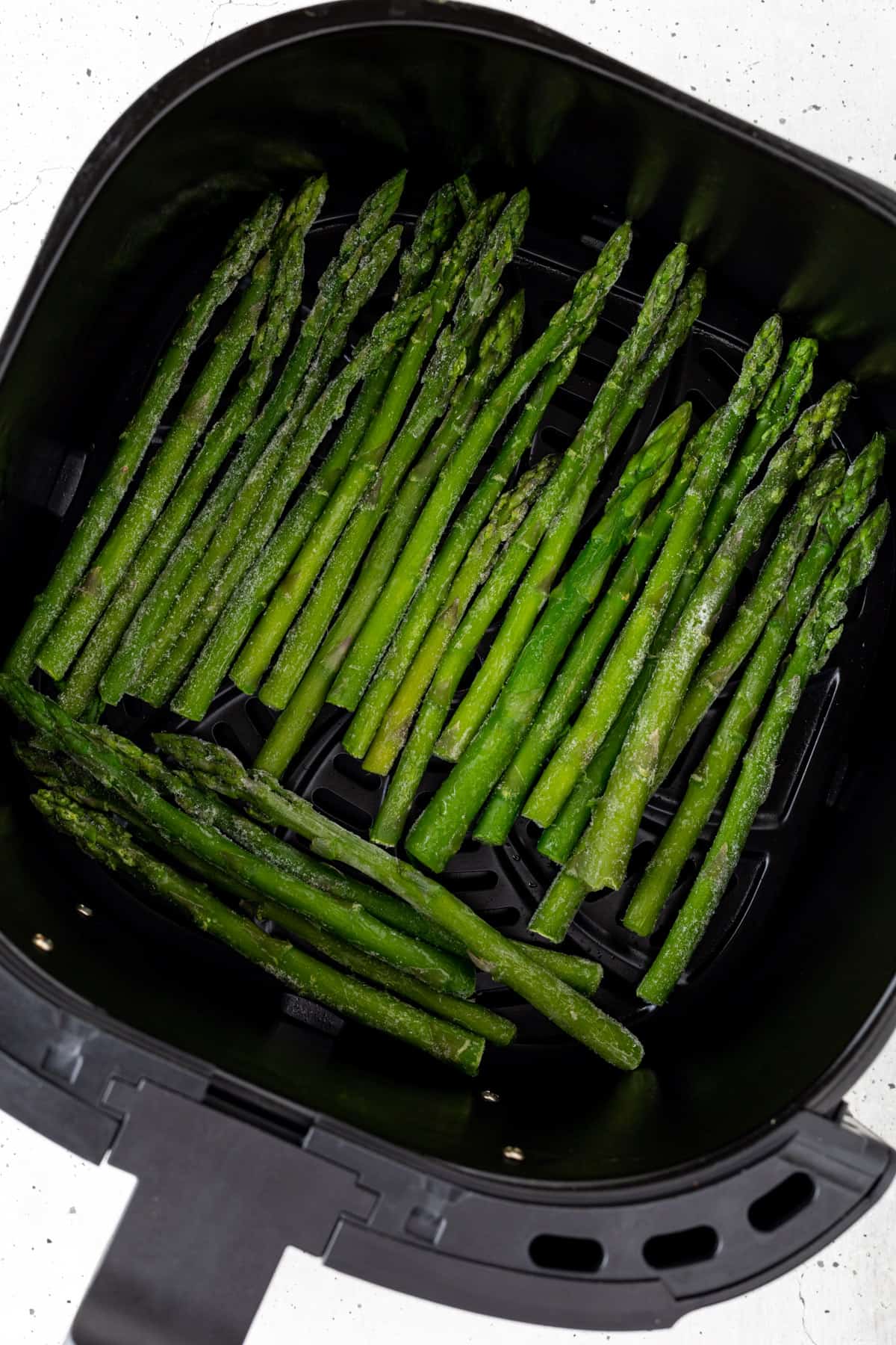 Uncooked frozen asparagus in an air fryer basket.