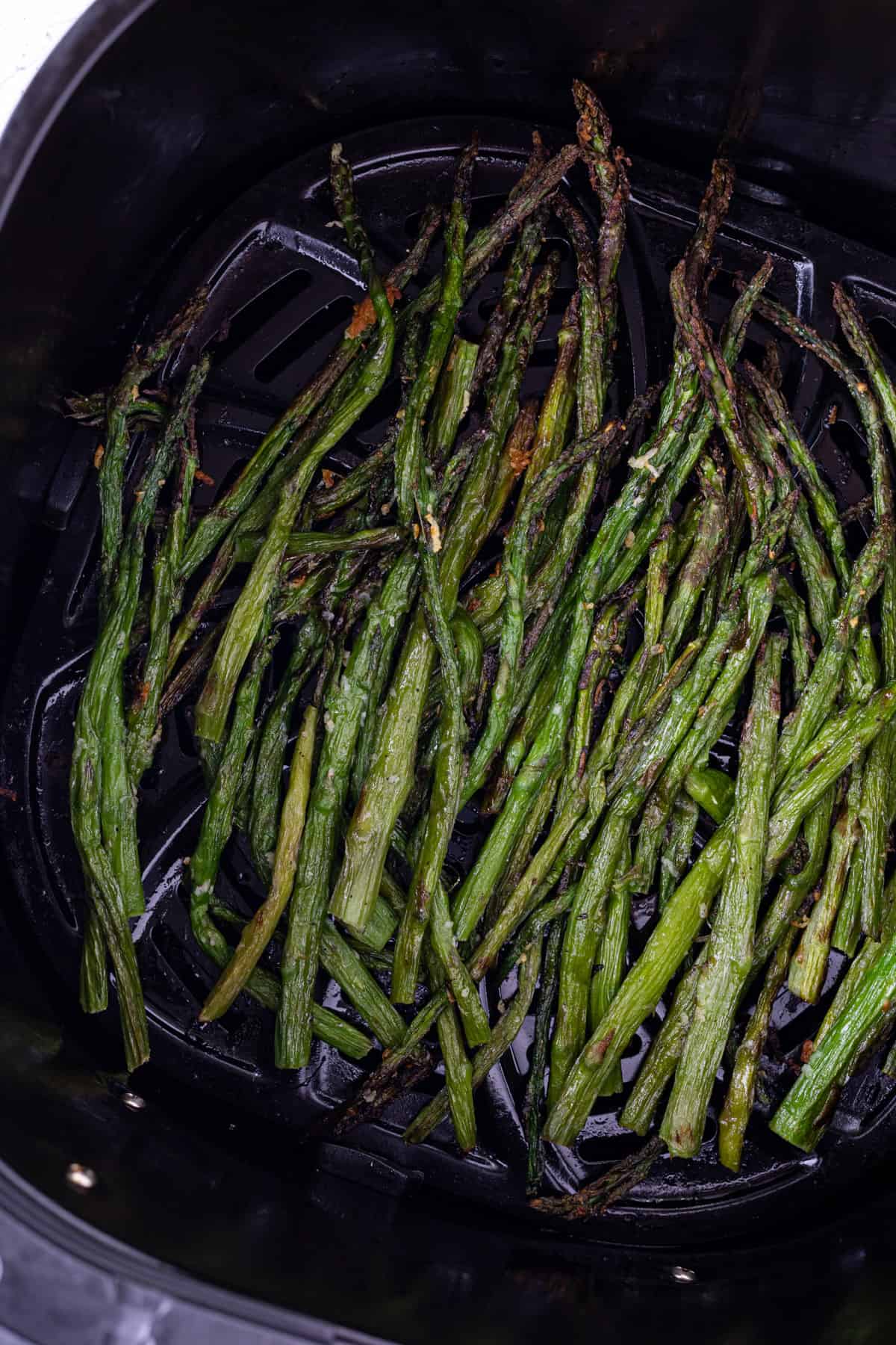Crispy asparagus in an air fryer basket.