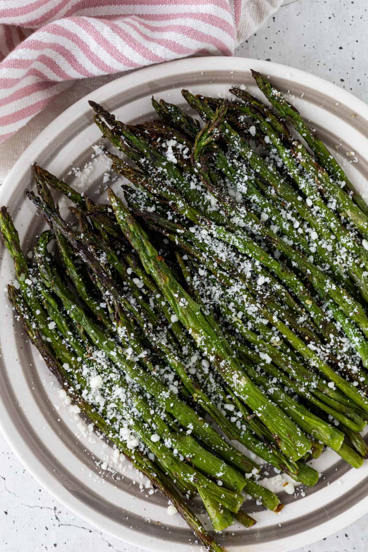 A plate of air-fried asparagus garnished with parmesan cheese.