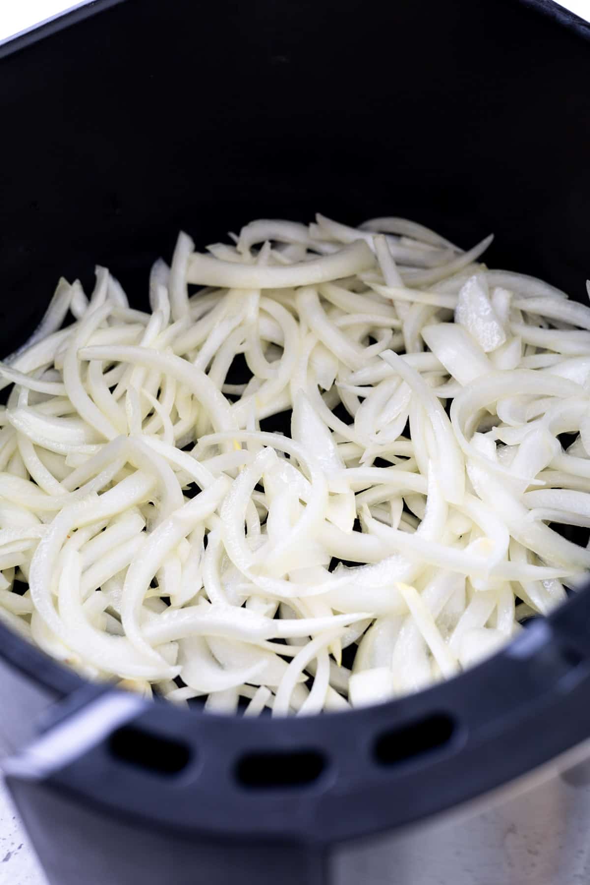 Oil-coated raw onion slices in an air fryer basket.