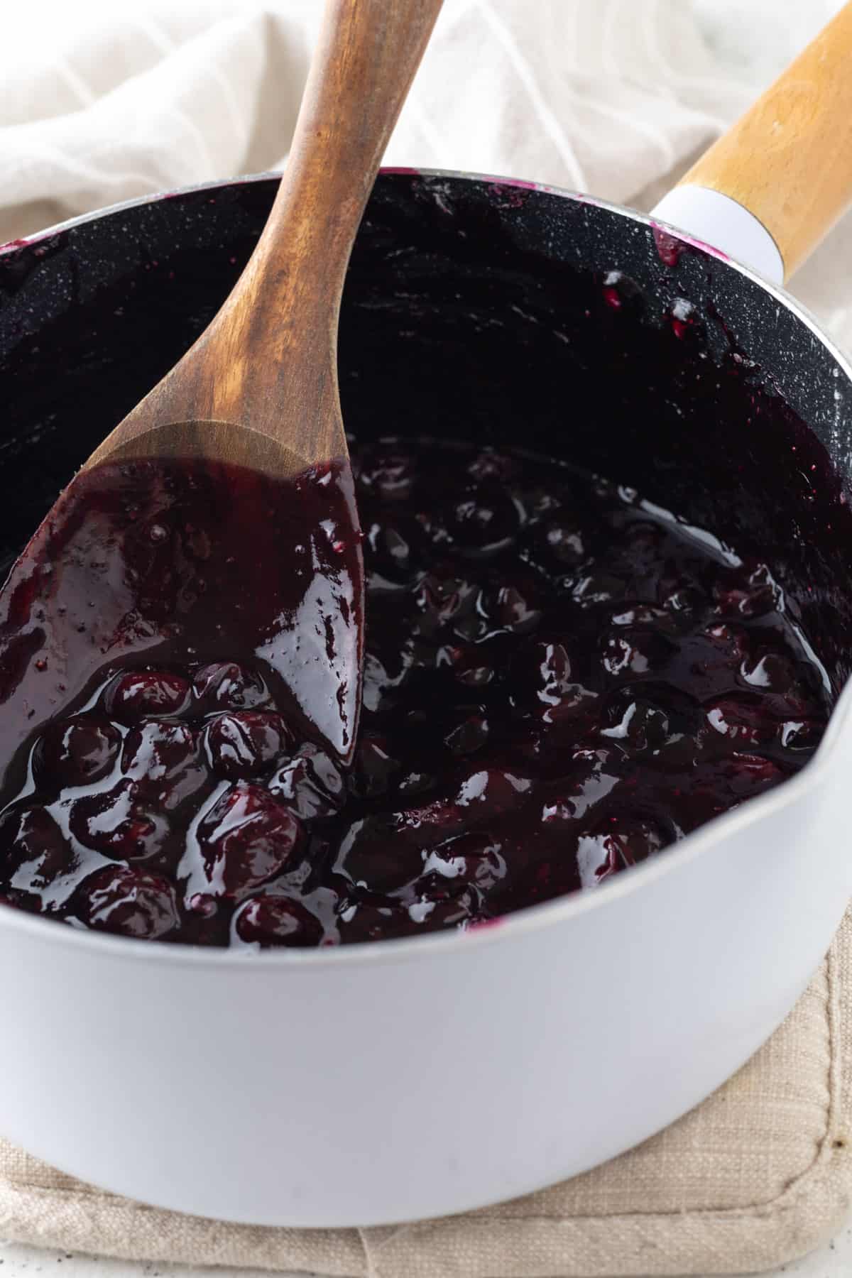 Blueberry filling in a saucepan with a wooden spoon.