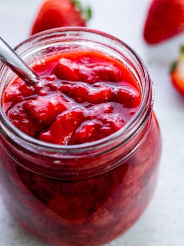 A jar of strawberry compote with a spoon.