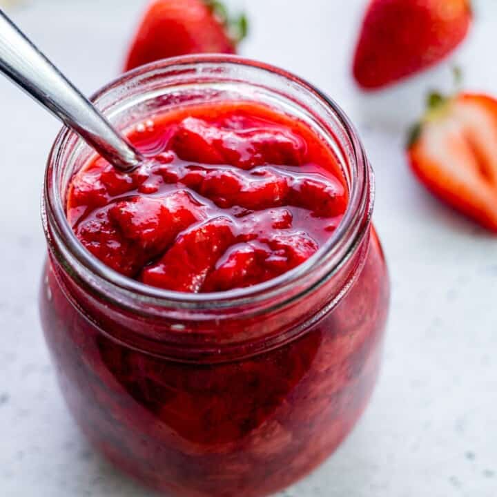 A jar of strawberry compote with a spoon.