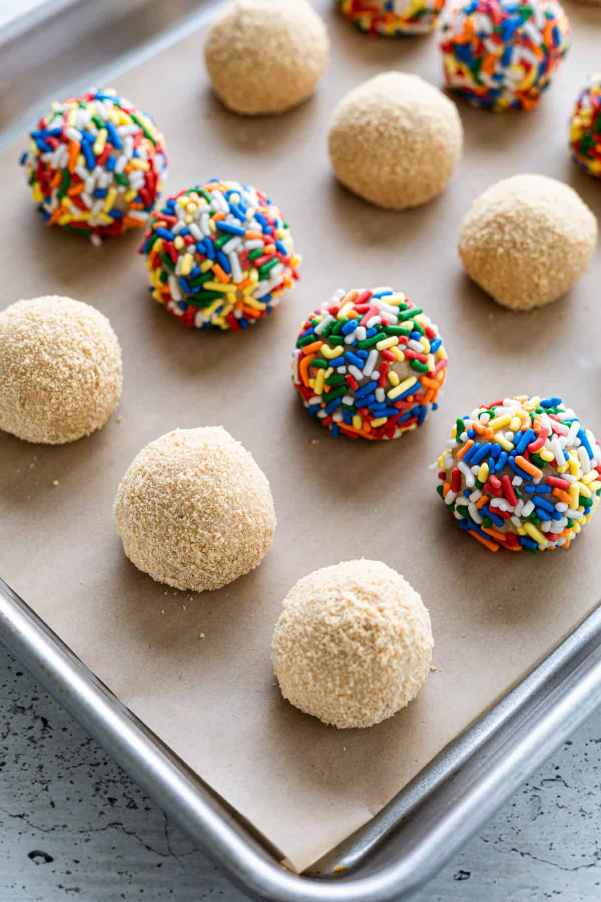 Cheesecake balls coated in toppings on a parchment-lined tray.