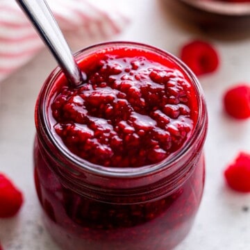 A jar of raspberry compote with a spoon.