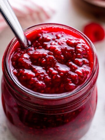 A jar of raspberry compote with a spoon.