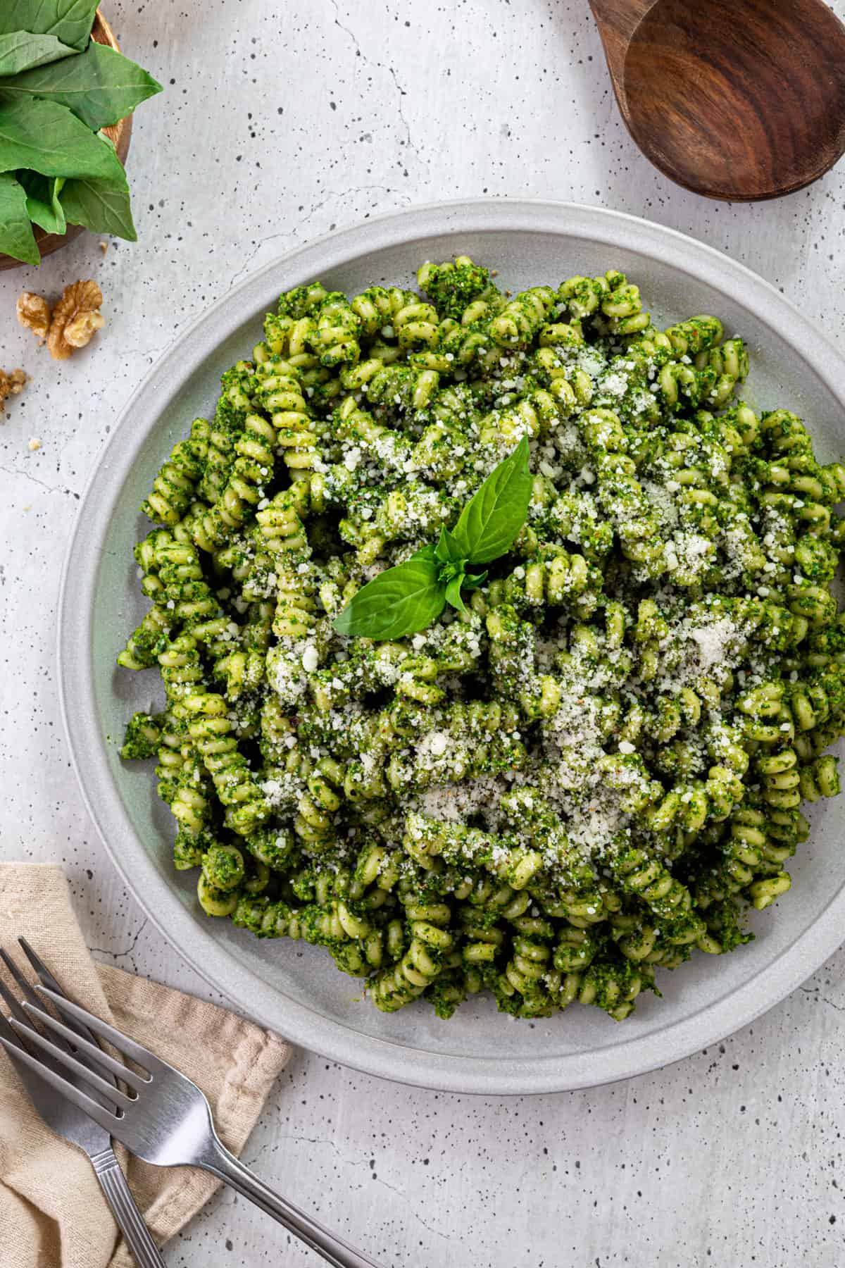 A plate of spinach pesto pasta with parmesan cheese and fresh basil.
