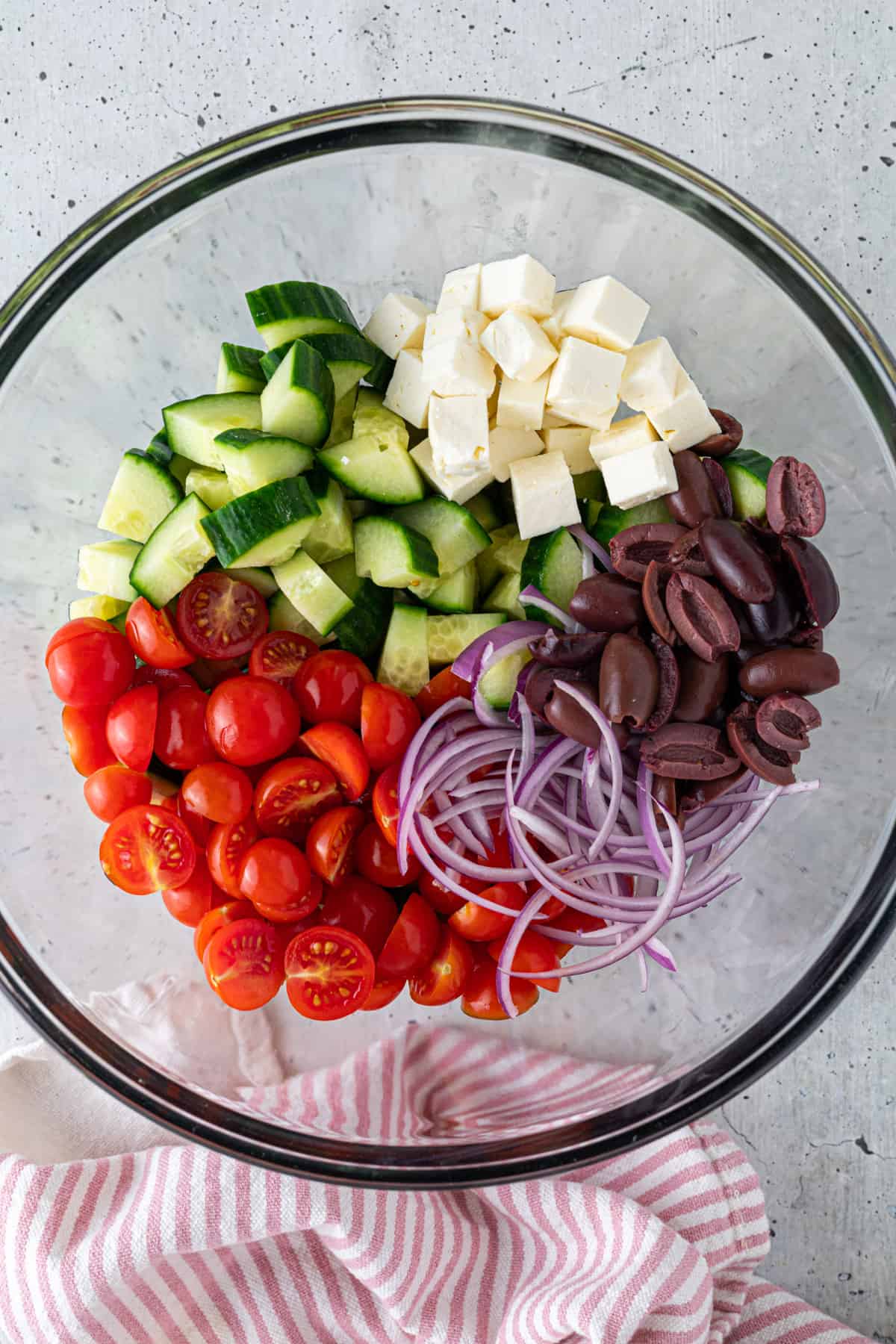 Fresh vegetables, olives, and feta cheese cubes in a large mixing bowl.