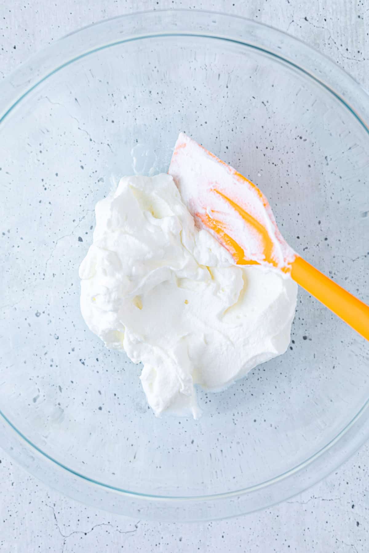 Whipped cream in a medium bowl with a rubber spatula.