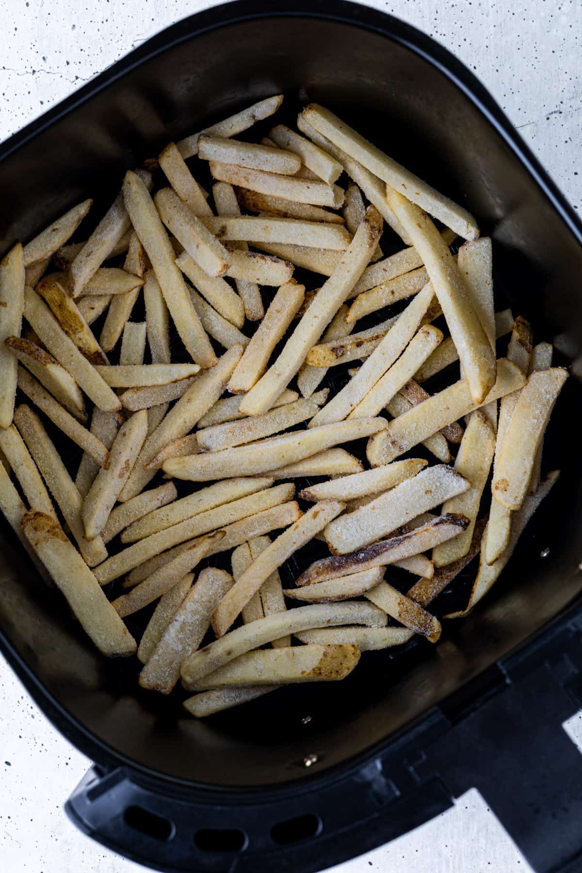Frozen fries in the basket of an air fryer.
