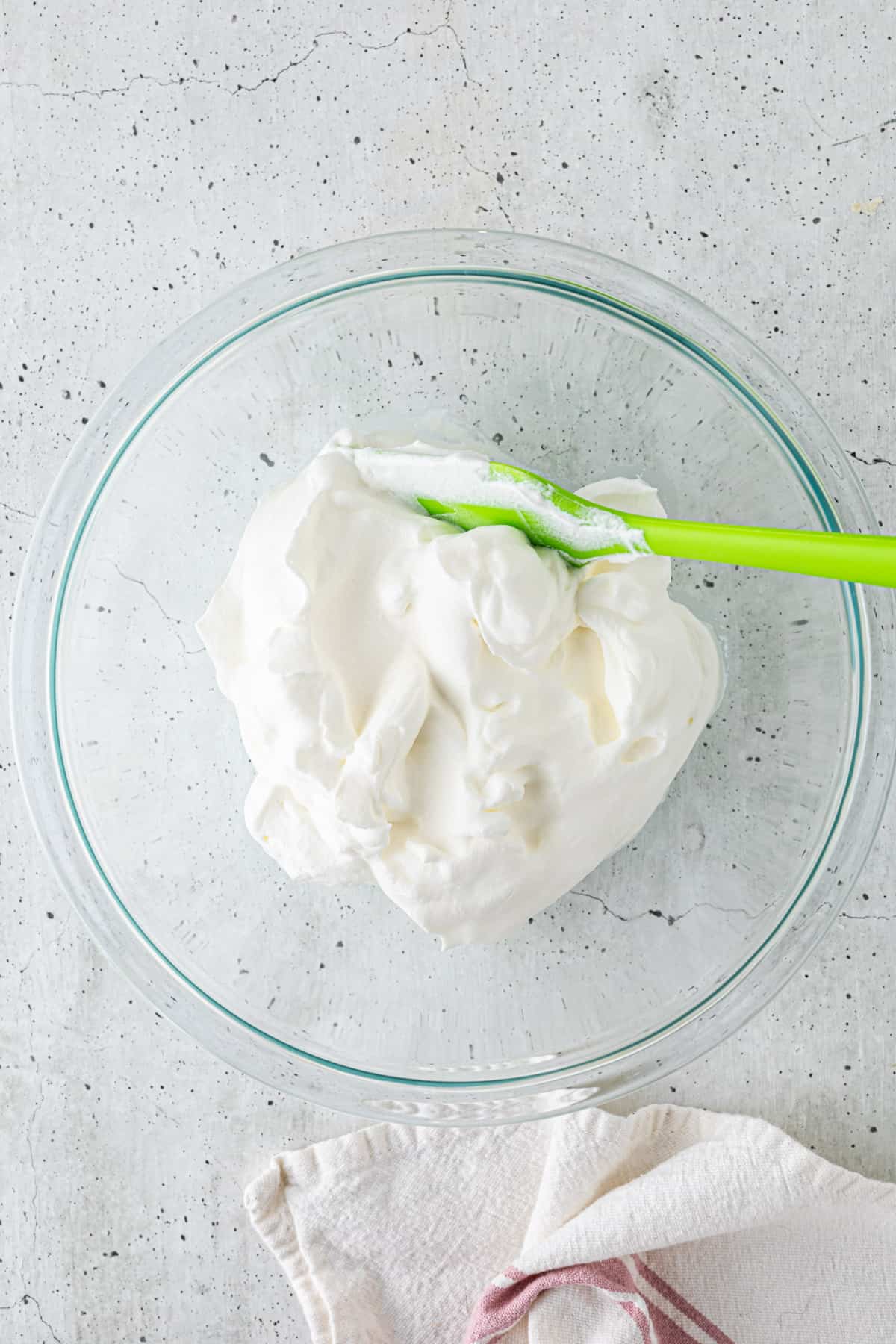 Whipped cream in a large bowl with a rubber spatula.